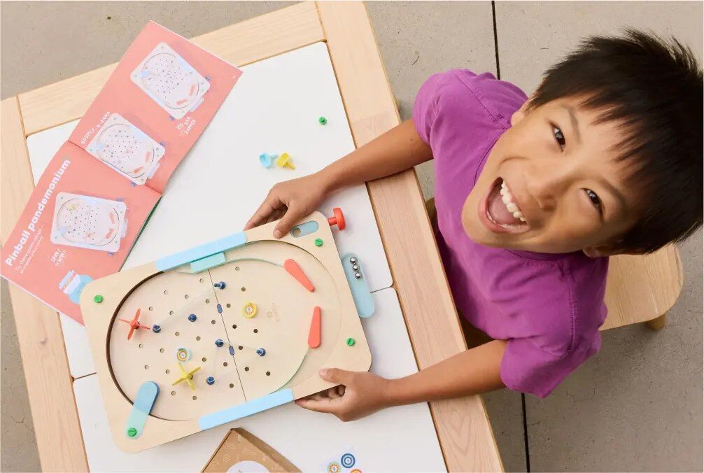 A child building a KiwiCo pinball project at a table