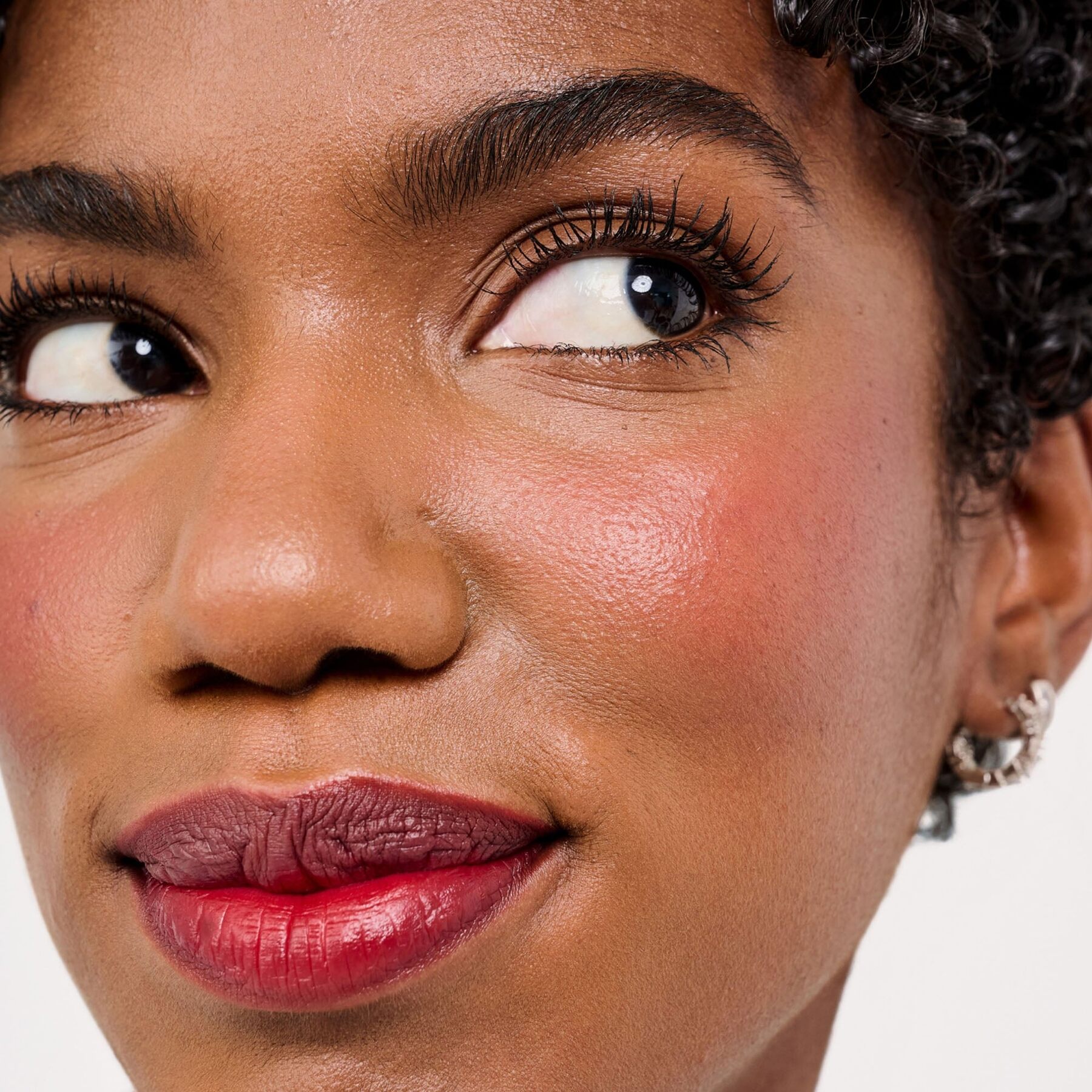 A close-up of a woman wearing a rosy lip and cheek tint, the look created by Benetint