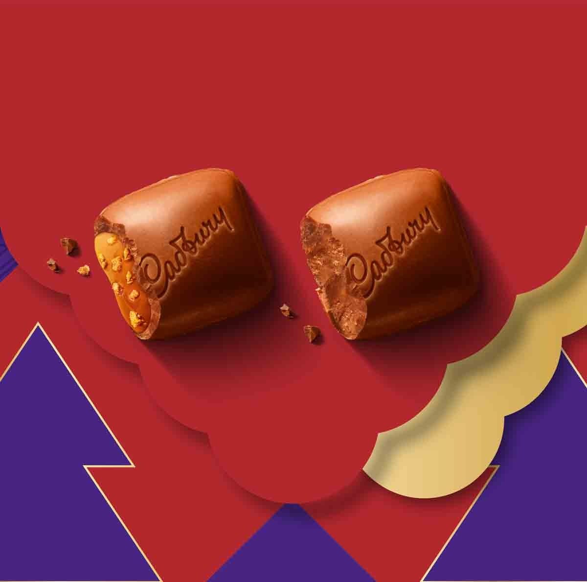 Two Cadbury Dairy Milk squares with Biscoff pieces on a red and purple festive background