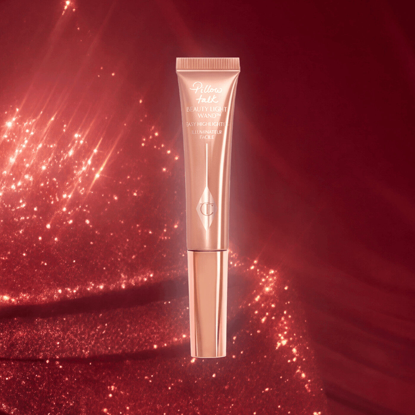 The Charlotte Tilbury Hollywood Beauty Light Wand in Pillow Talk Original on a red glitter background