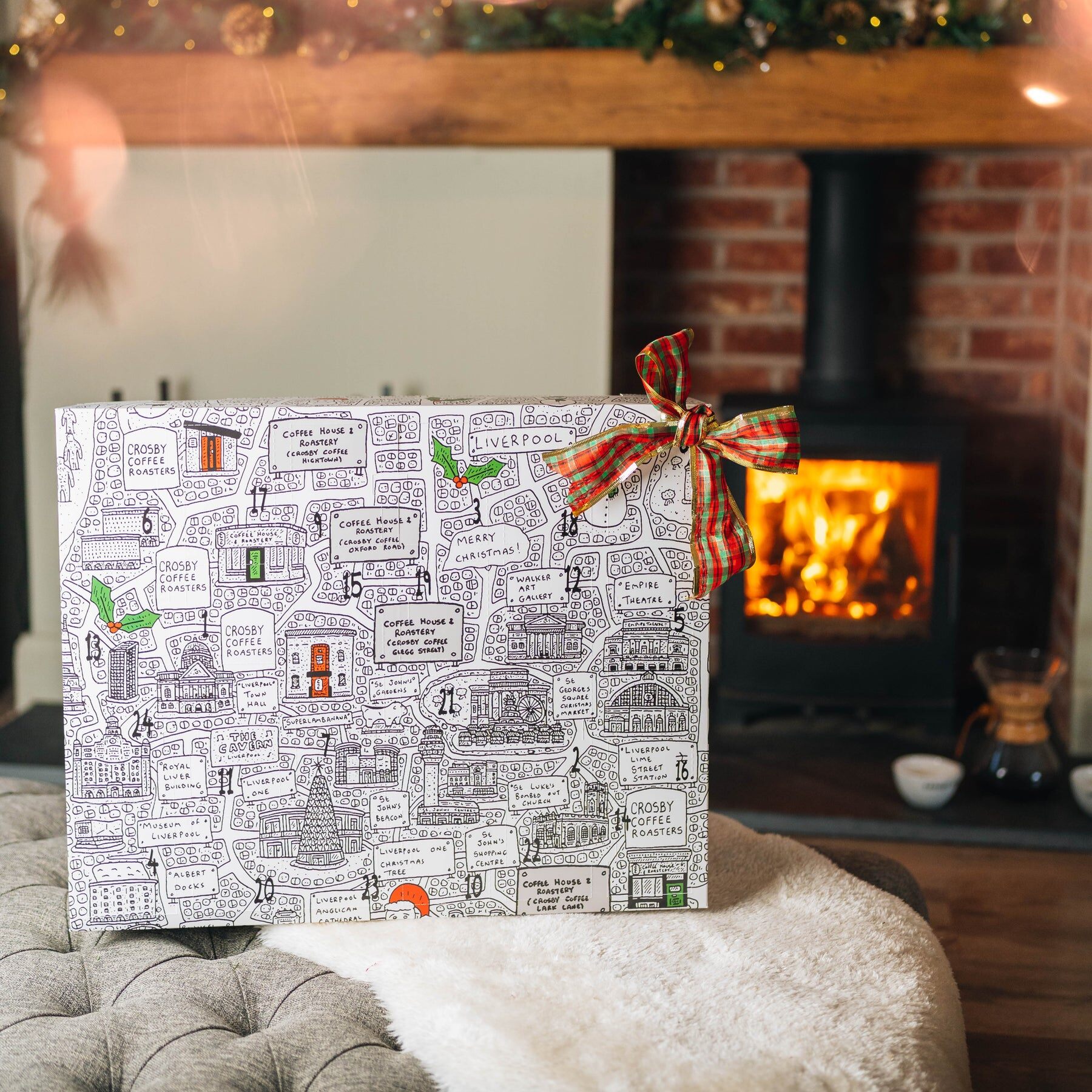 The Crosby Coffee advent calendar box, covered in black and white doodles, on a cushion in front of a log fire
