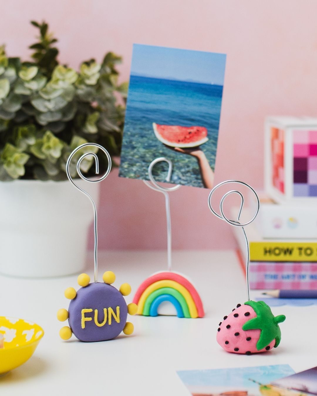 Three clay photo holders shaped like a purple disc reading FUN, a rainbow and a strawberry, holding photos on wire stands
