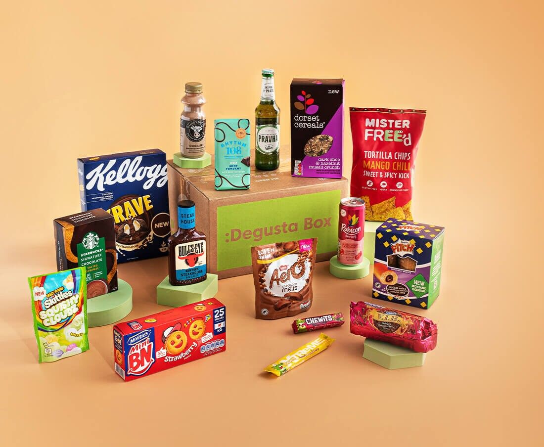 A Degusta Box surrounded by food and drink products including cereal, crisps, biscuits, sweets and drinks on an orange background