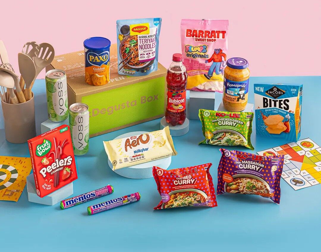 The September 2026 Degustabox contents laid out around the green and brown box, including noodles, crisps, sweets, drinks and a jar of curry sauce