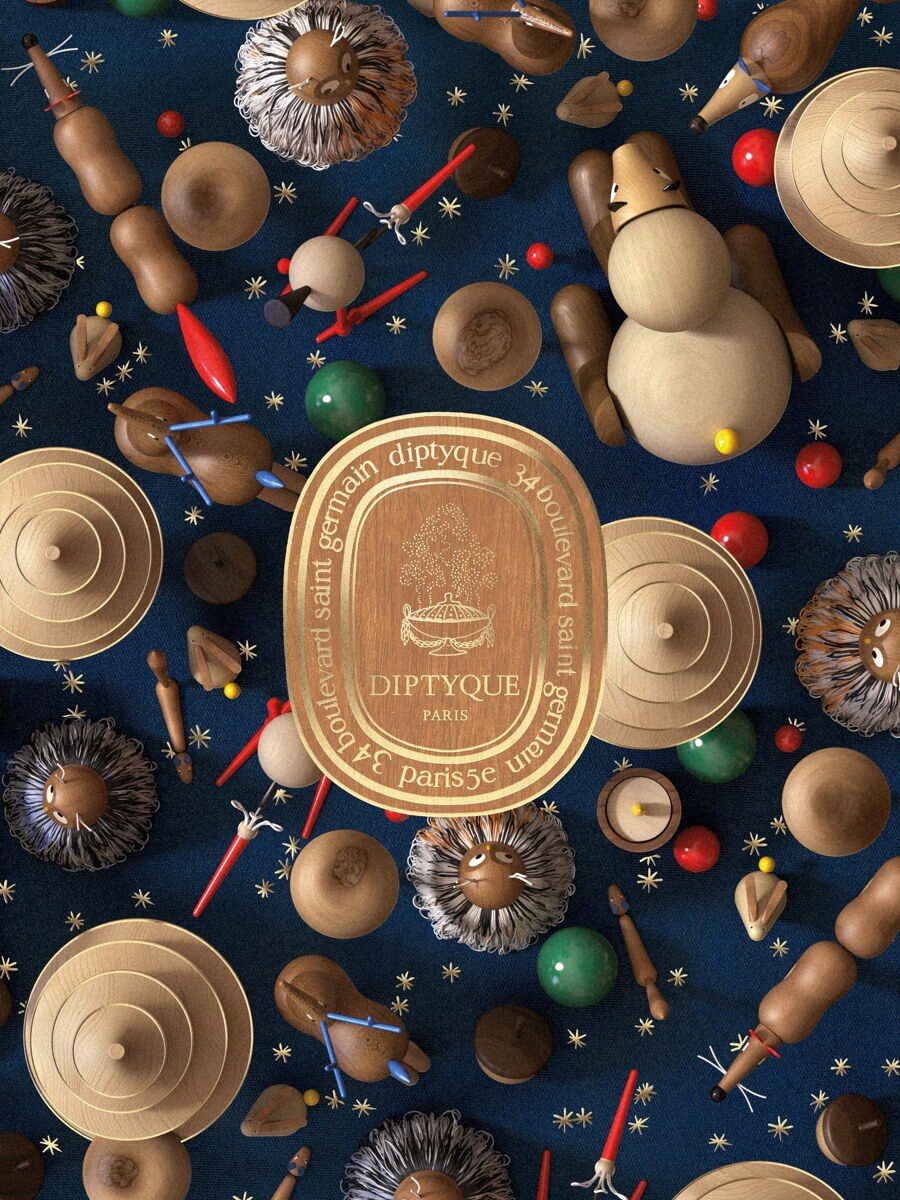 A gold Diptyque candle surrounded by wooden Christmas decorations on a dark blue background