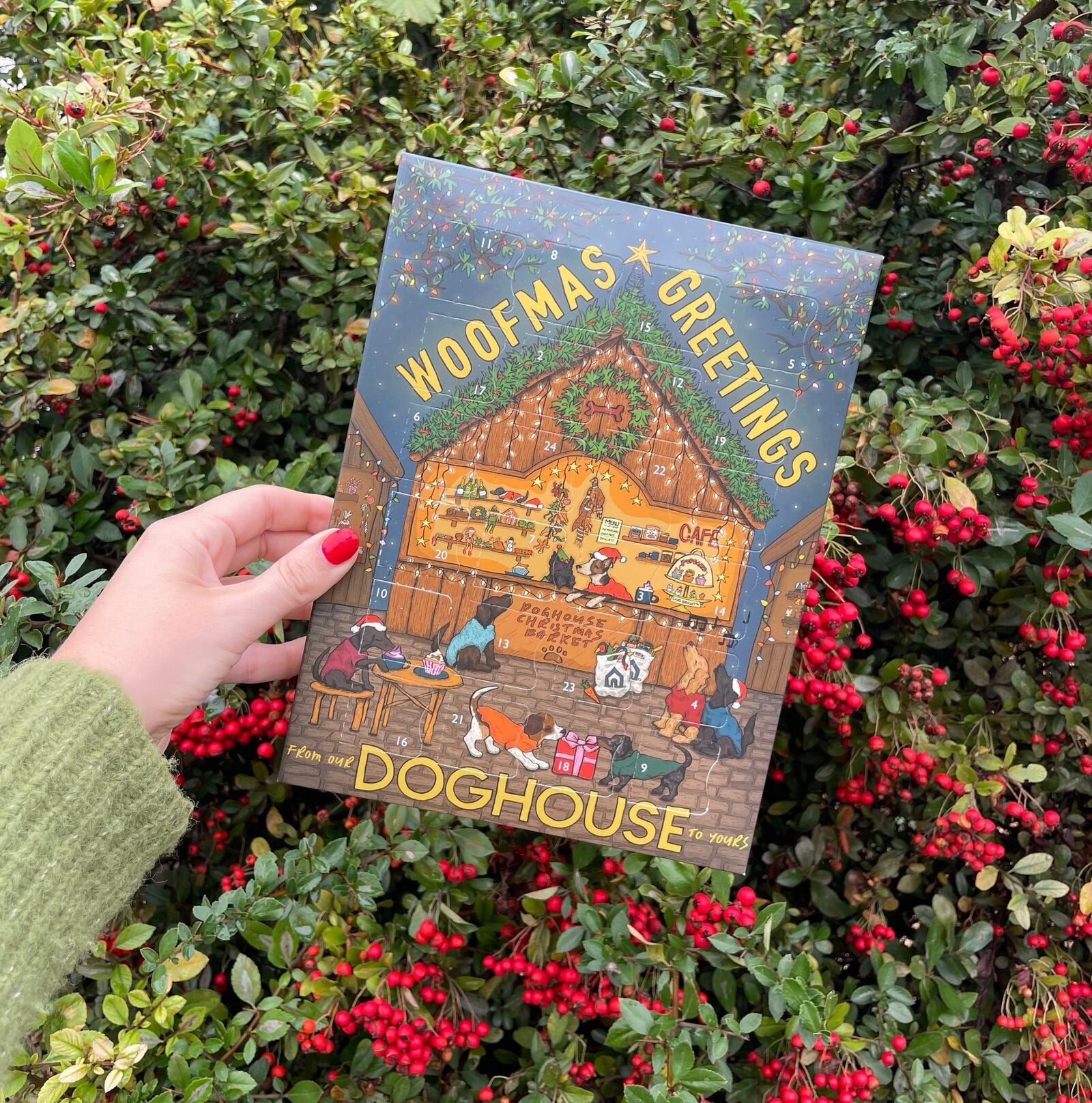 A hand holding the Doghouse Woofmas Greetings dog advent calendar over autumn leaves