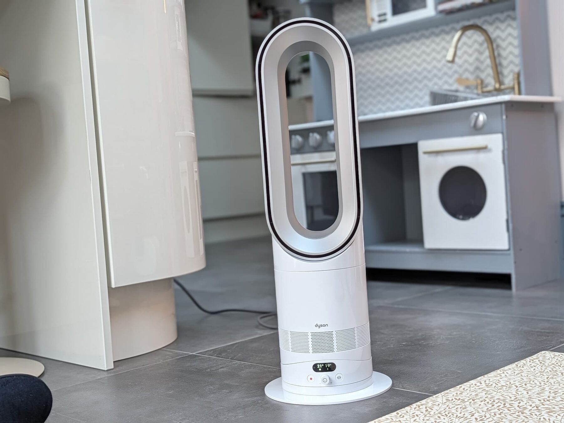 Dyson Hot+Cool HF1 heater and cooling fan standing on a grey floor in a room, next to a white cupboard