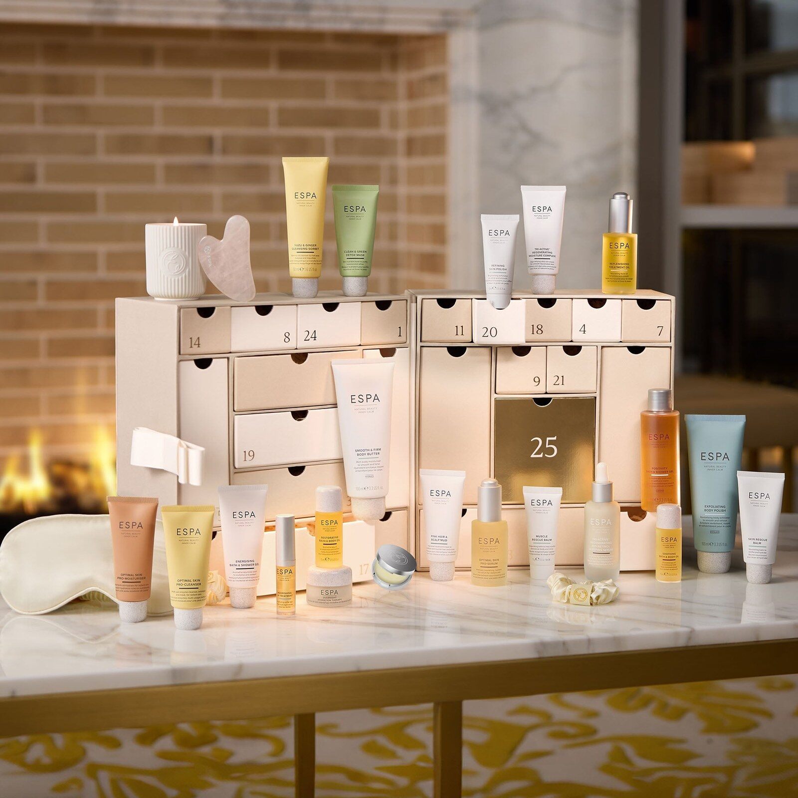 The ESPA Moments of Wellness advent calendar open on a marble table, its cream drawers surrounded by ESPA bottles and tubes in front of a fireplace