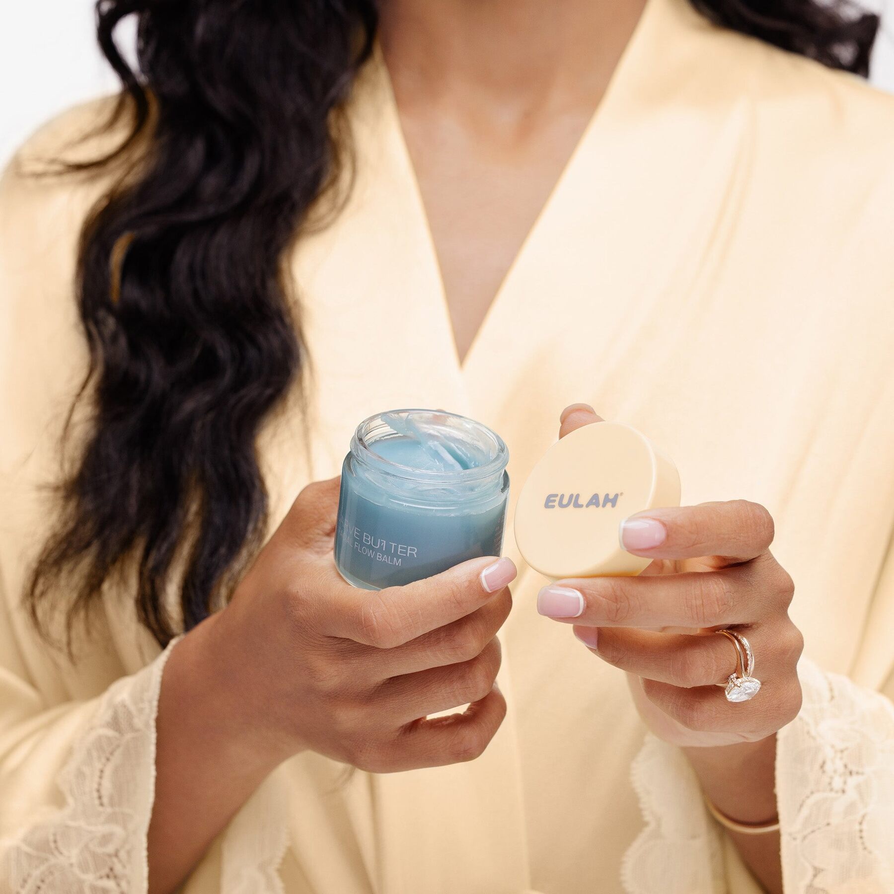 A woman in a cream robe holding a jar of blue Eulah Carve Butter balm