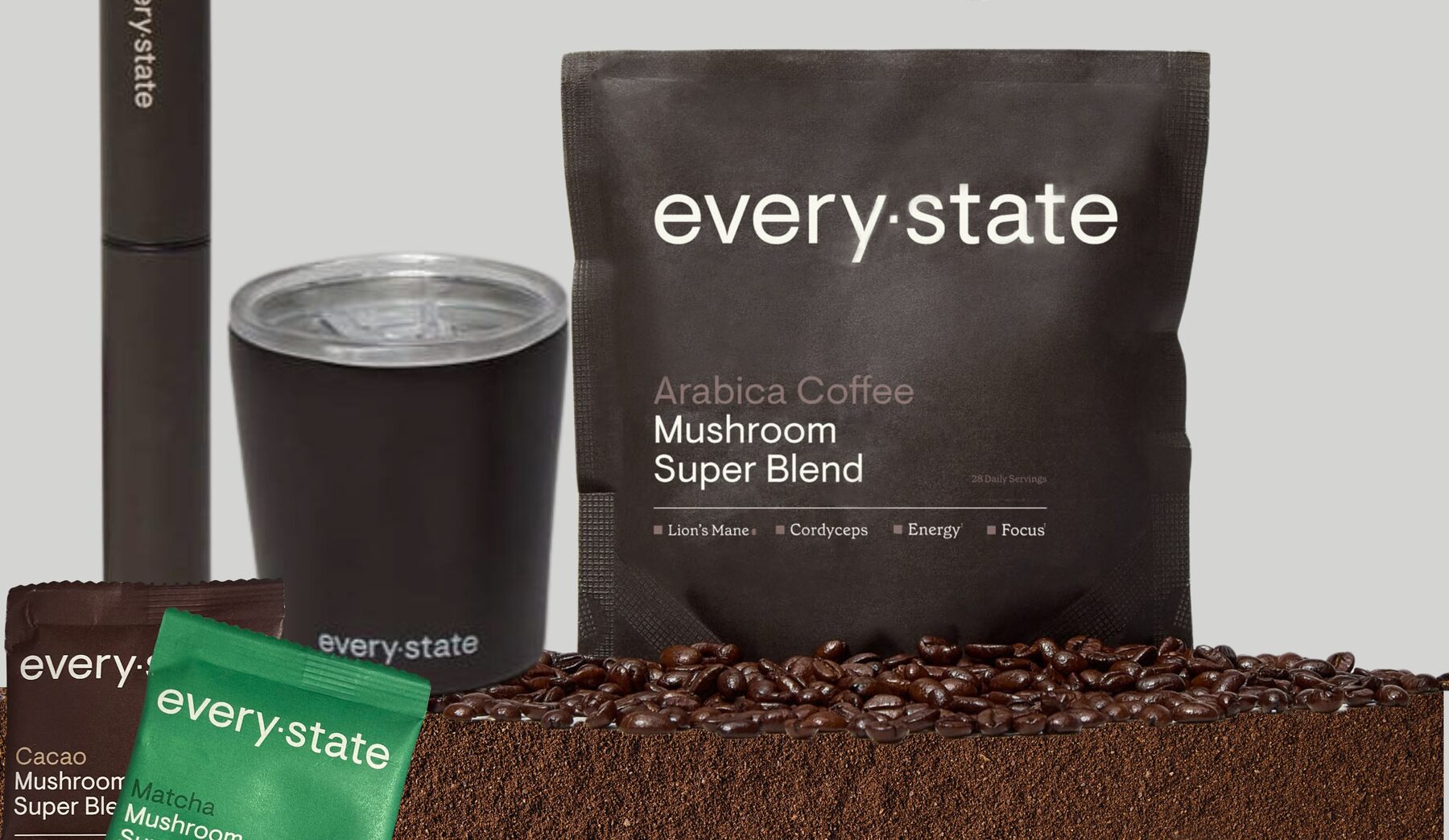 The everystate starter kit with a dark pouch of Arabica Coffee + Mushroom Super Blend, a black cup, a whisk and sample sachets on coffee beans