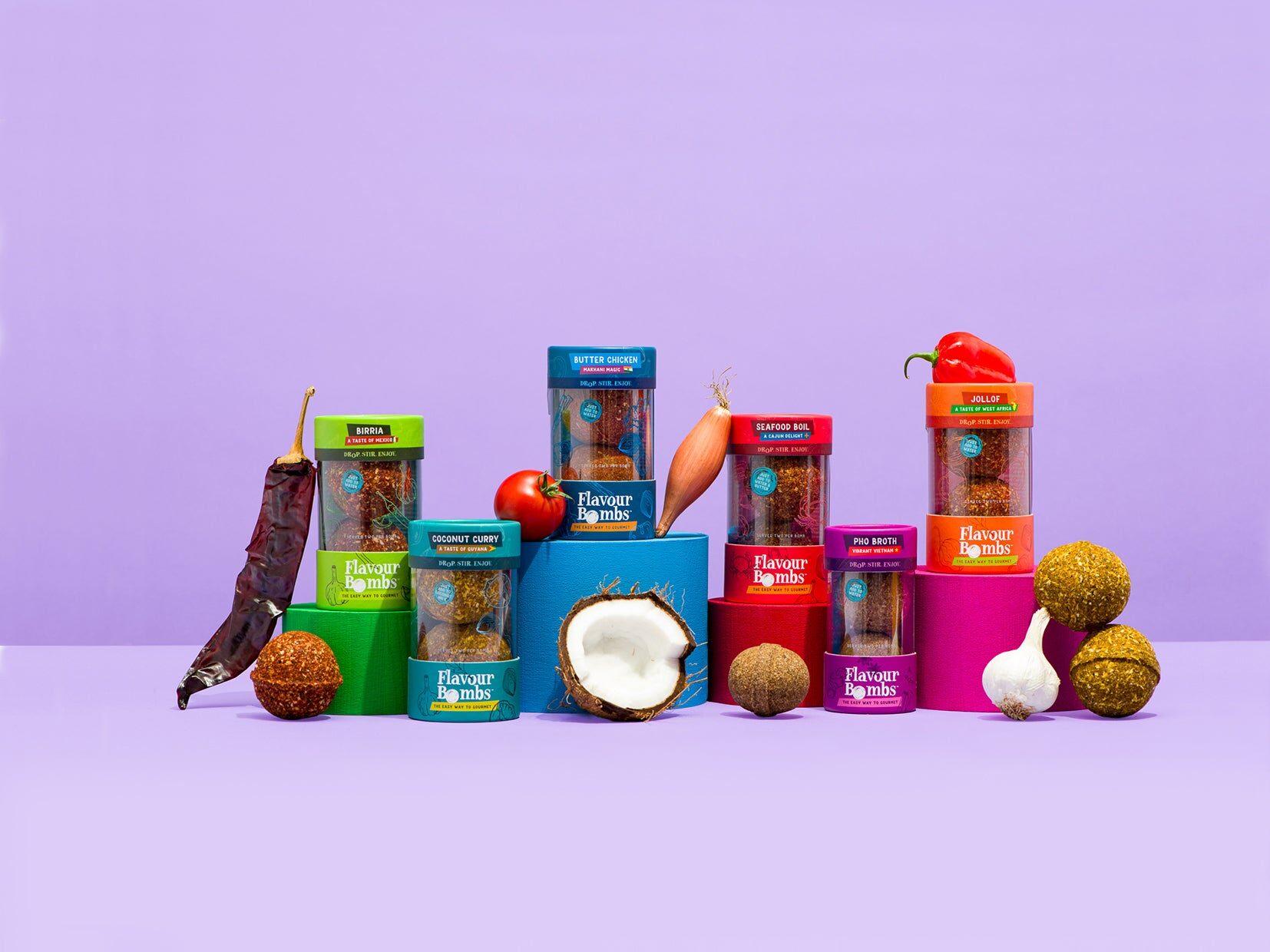 The Flavour Bombs range of jars stacked on a lilac background with chillies, garlic and coconuts