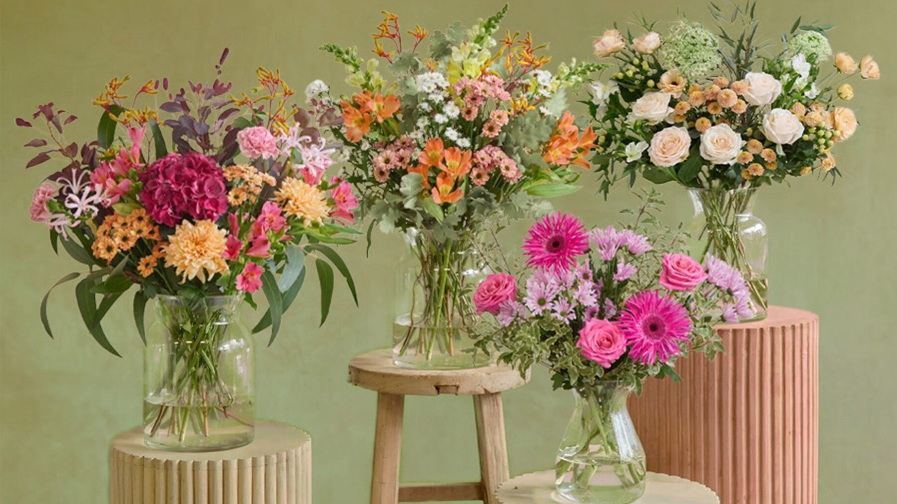 Three Freddie's Flowers bouquets in glass vases on stools against a green wall