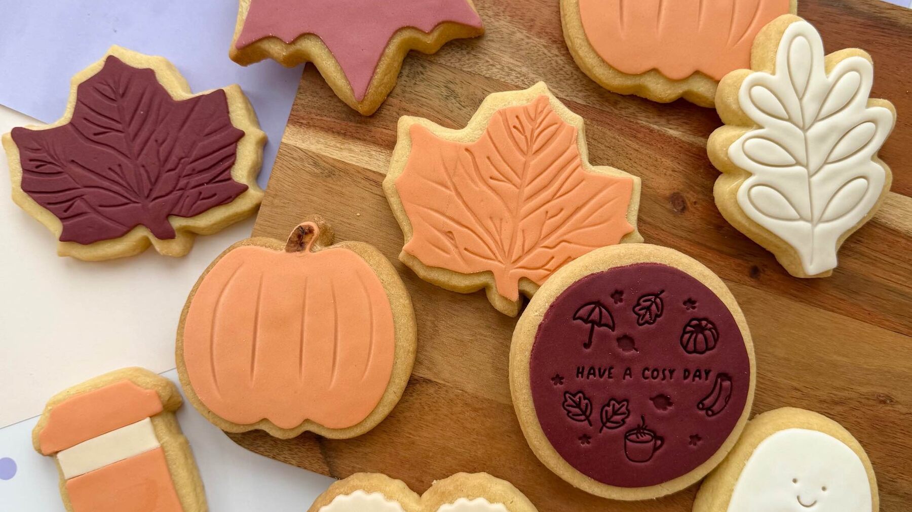 Iced autumn cookies in maple leaf, pumpkin and ghost shapes on a wooden board