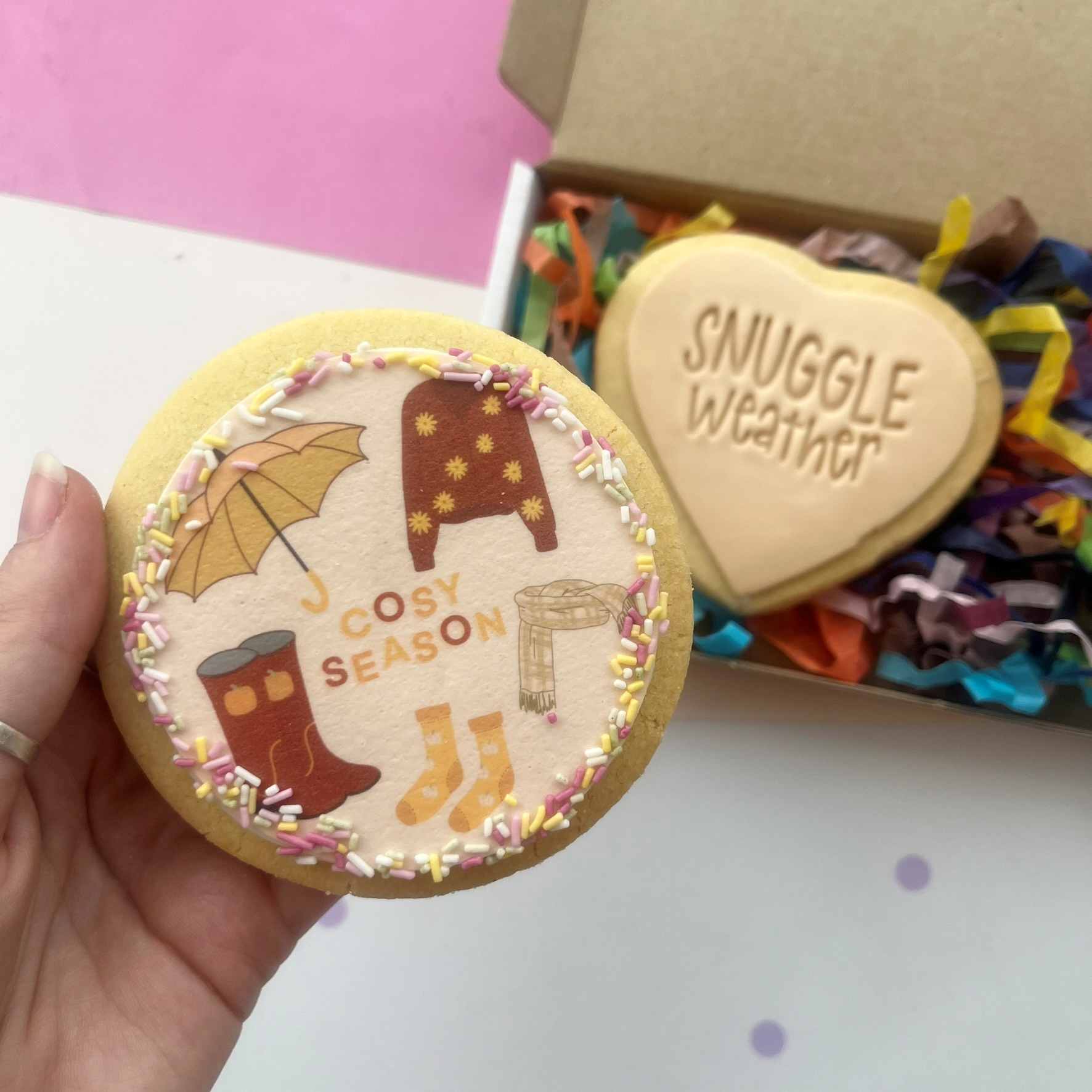 A Cosy Season cookie with boots, socks and a scarf beside a Snuggle Weather heart cookie