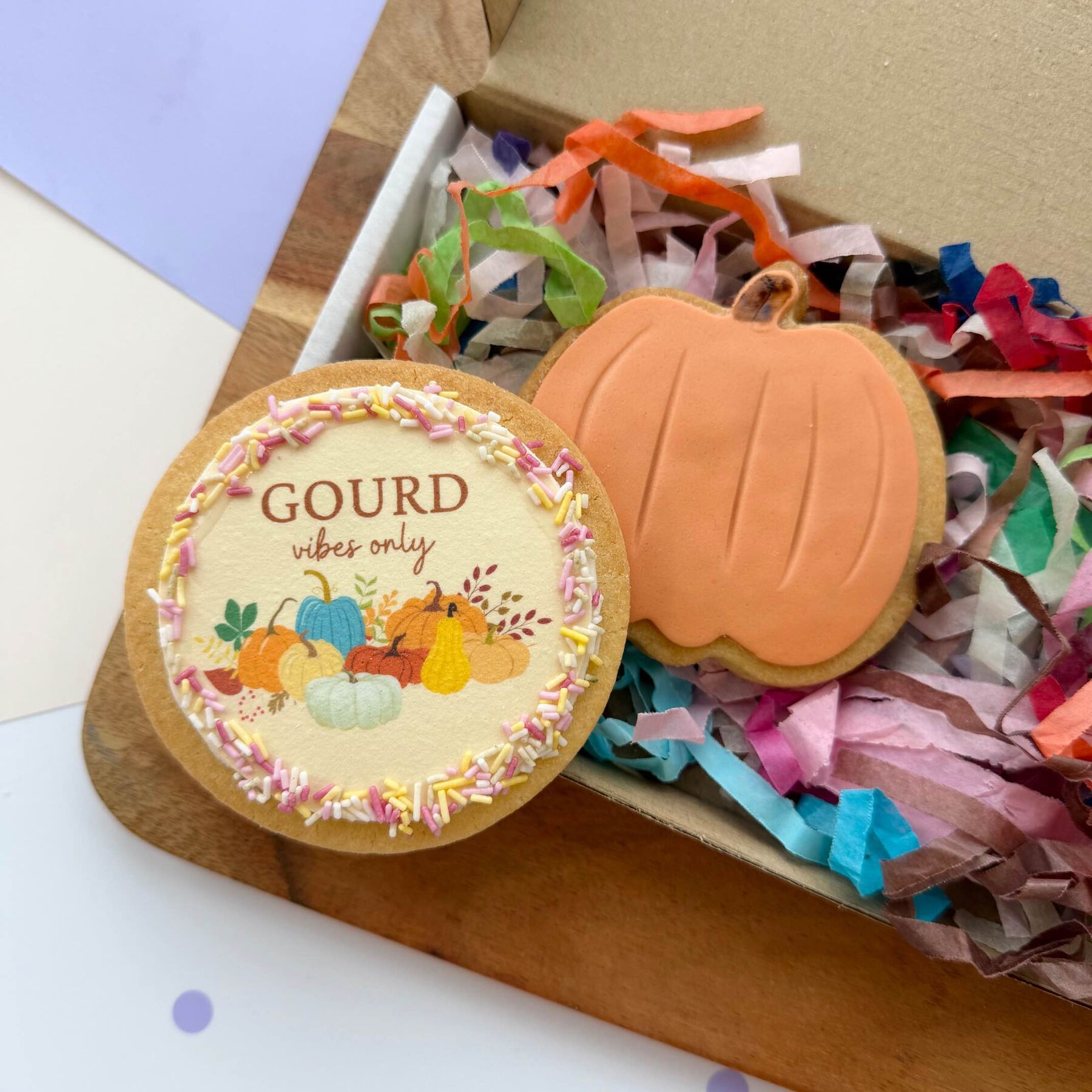 A Gourd Vibes Only cookie beside an orange pumpkin cookie in a gift box