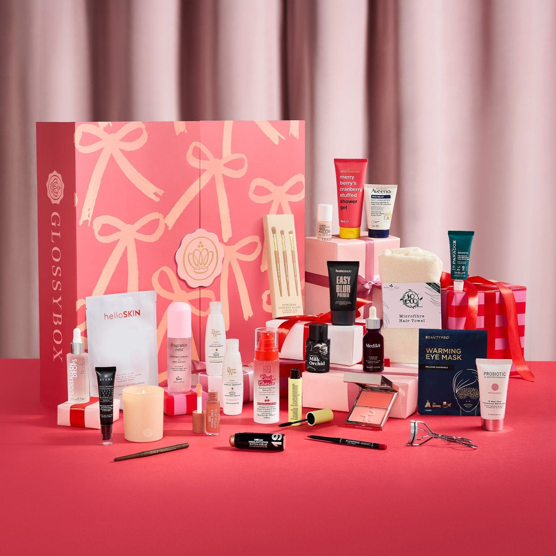 The GLOSSYBOX Beauty Wrapped advent calendar 2026 open with its beauty products laid out in front of red curtains