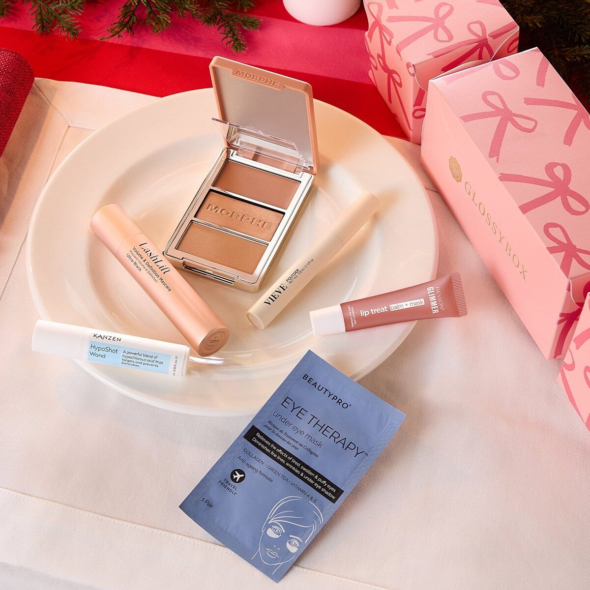 The GLOSSYBOX Christmas Cracker 2026 products on a festive table with an open face palette, an eye mask and a lip balm
