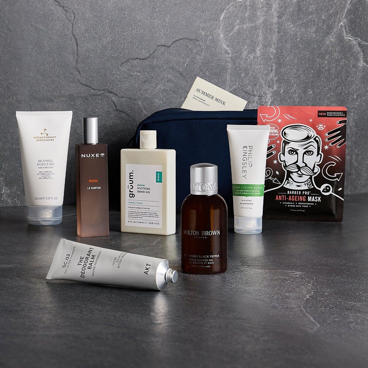 The GLOSSYBOX Grooming Kit 2026 with a navy wash bag, a Nuxe Men perfume, a Molton Brown shower gel and a Barber Pro face mask