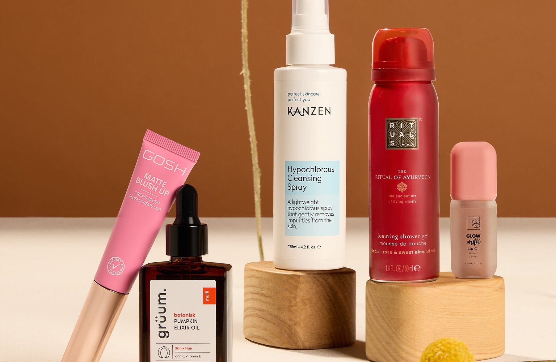 The five products of the GLOSSYBOX October 2026 box on a warm brown and cream background