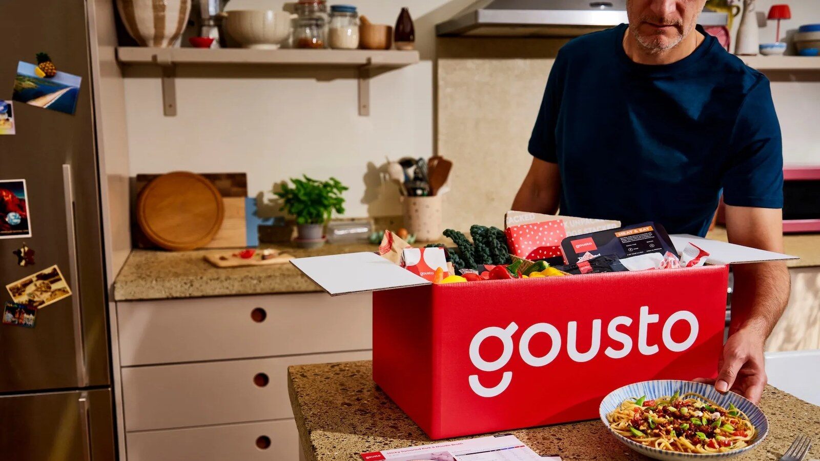 A man unpacking a red Gousto box on a kitchen worktop
