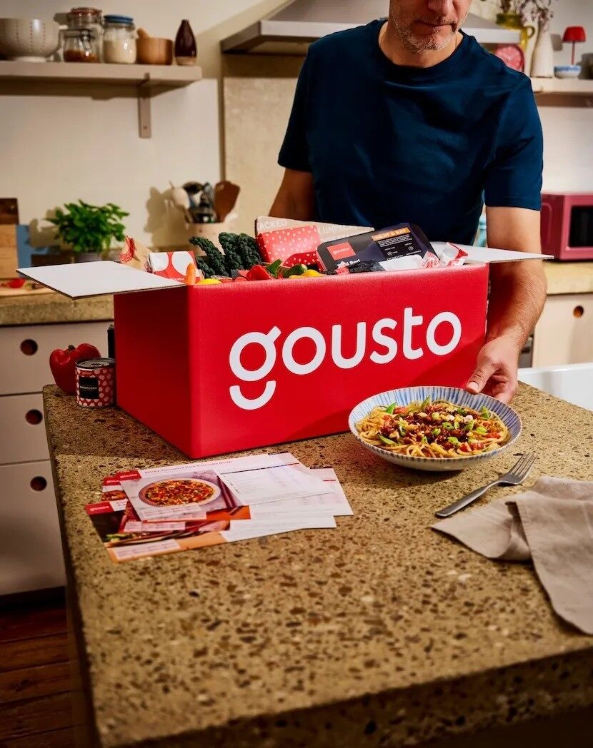 A man unpacking a red Gousto recipe box in a home kitchen