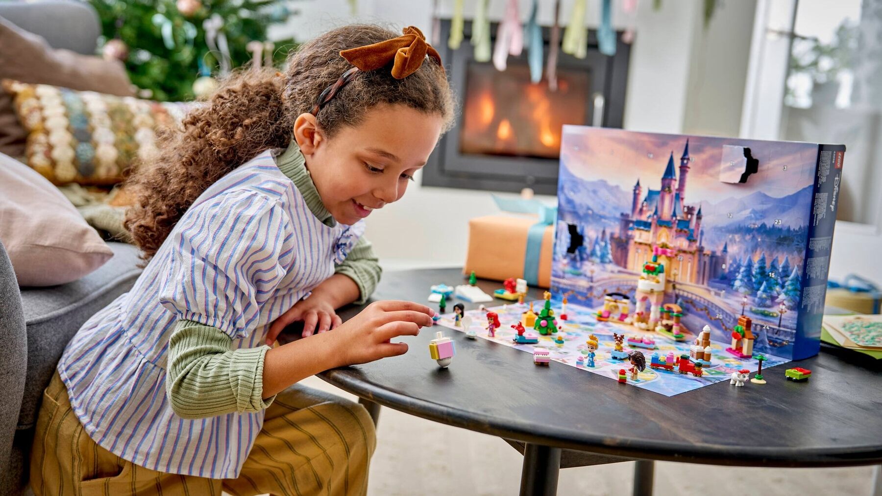 A girl building mini figures from the LEGO Disney Princess Advent Calendar on a table beside a Christmas tree