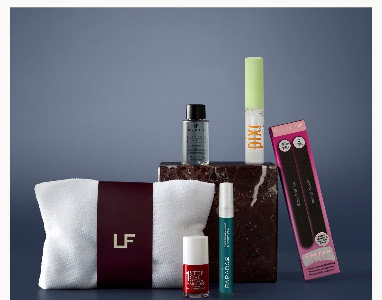 The LOOKFANTASTIC October 2026 beauty box products, including a white and burgundy hair wrap, a nail polish and a brow gel, on dark blue and marble blocks