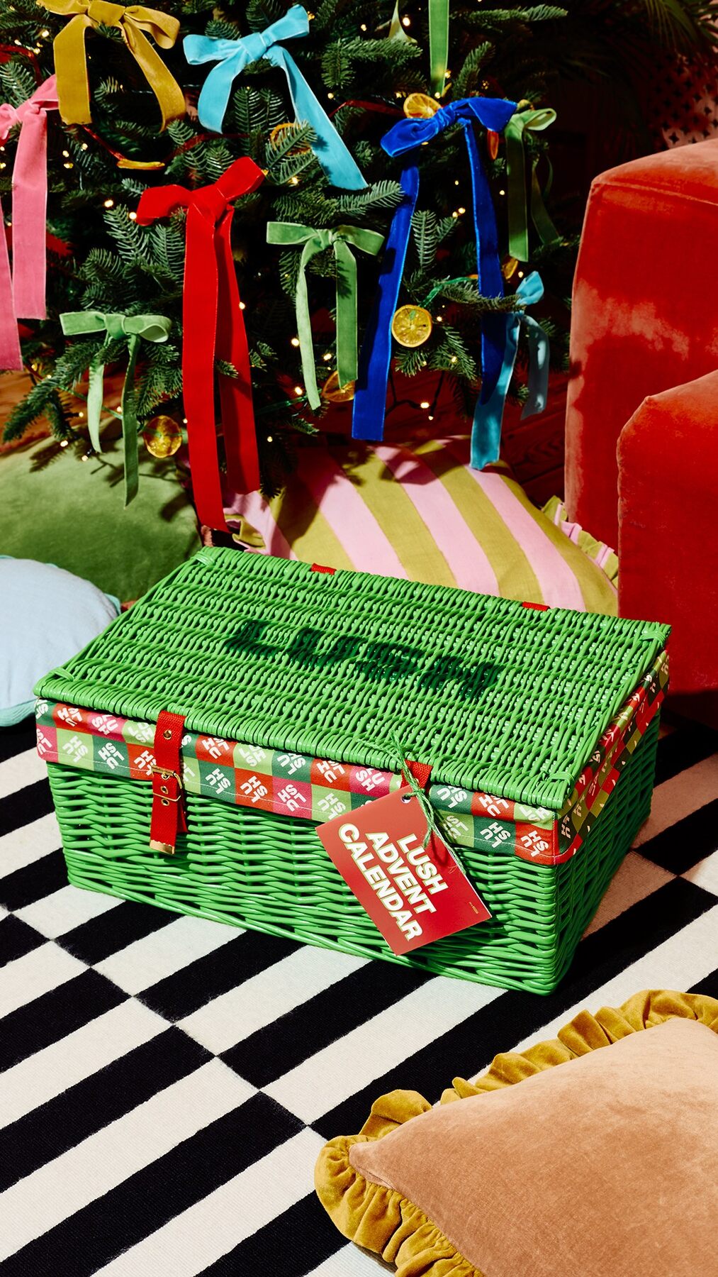 The green wicker Lush Advent Calendar 2026 hamper with red straps and a Lush gift tag in a festive living room