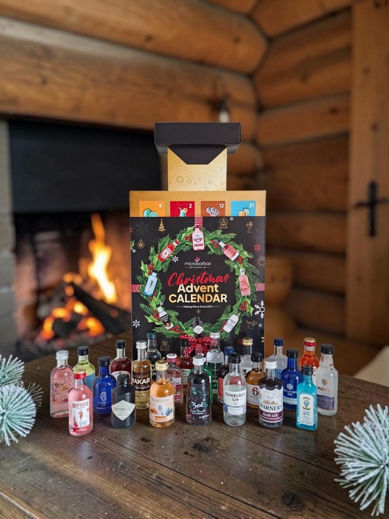 The MicroBarBox gin advent calendar with a Christmas wreath design, surrounded by its gin miniatures in front of a fireplace