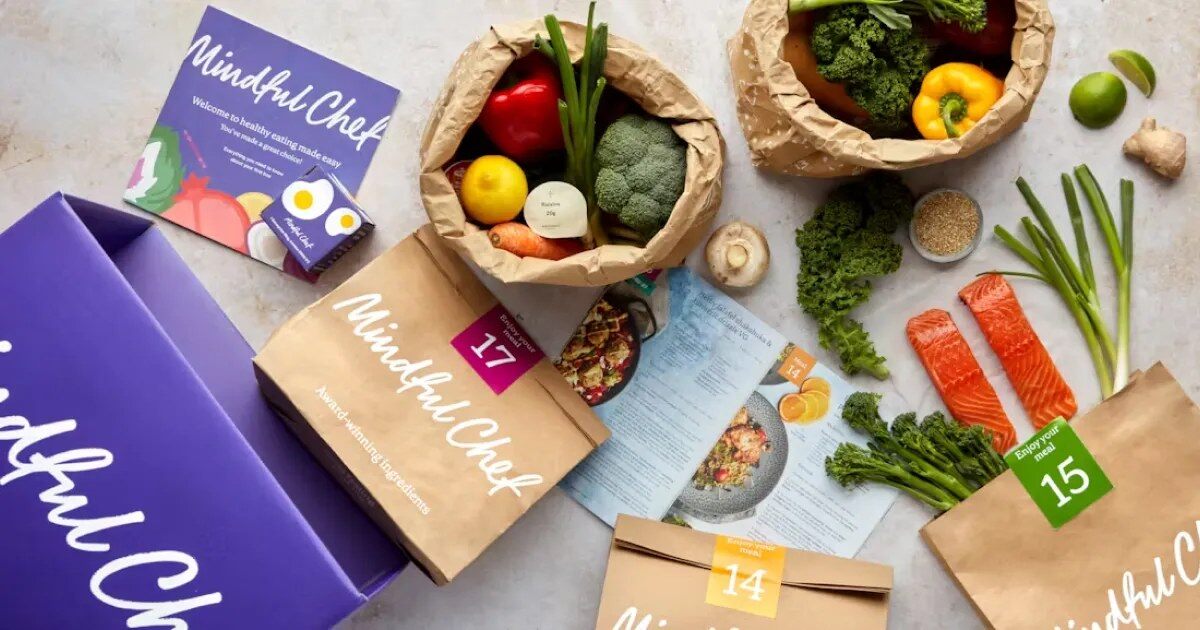 A purple Mindful Chef recipe box with numbered recipe bags, fresh vegetables and salmon laid out around it