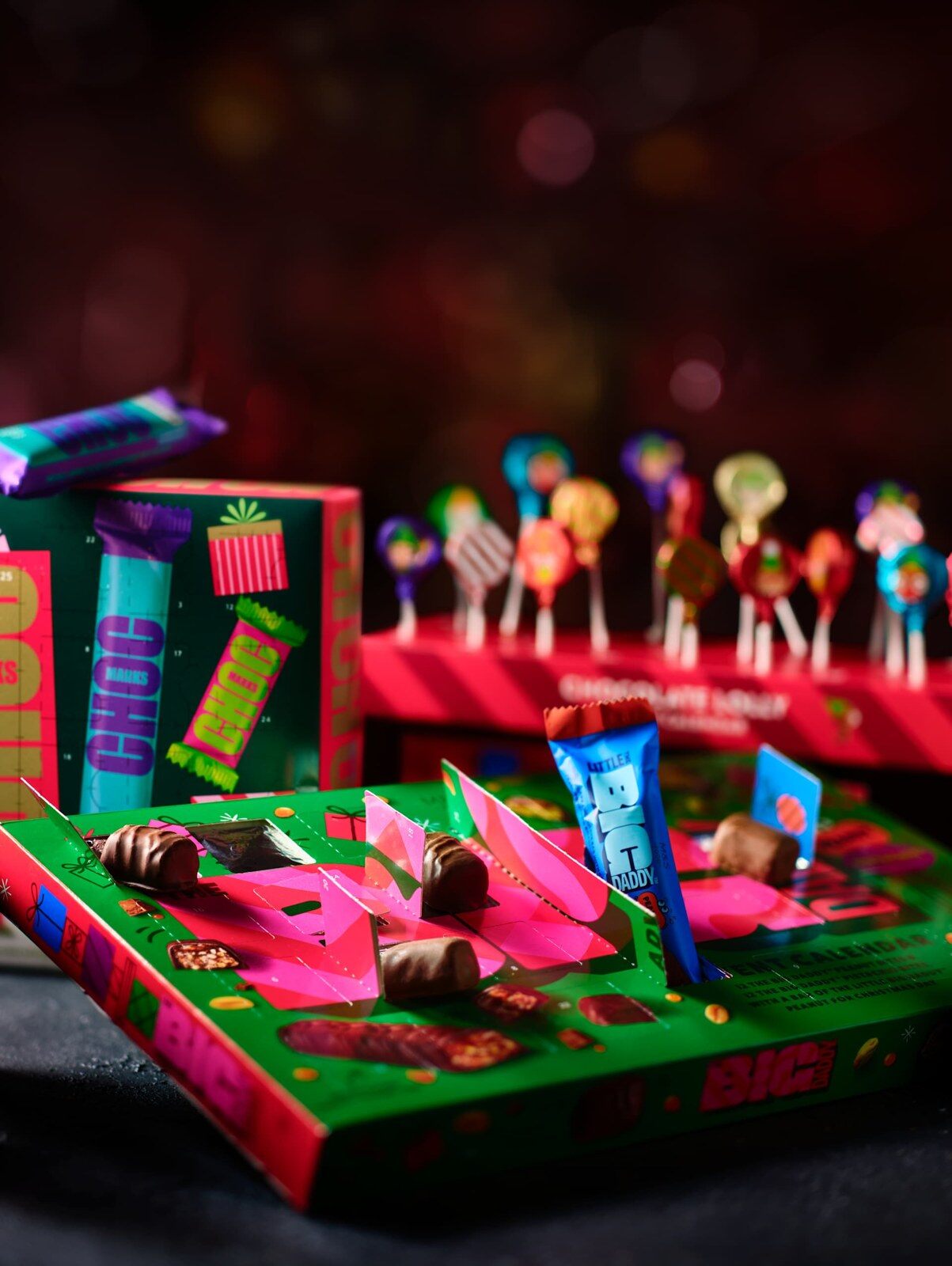 The Big Daddy advent calendar open on a dark table, with wrapped chocolate bites in the drawer and festive lights behind