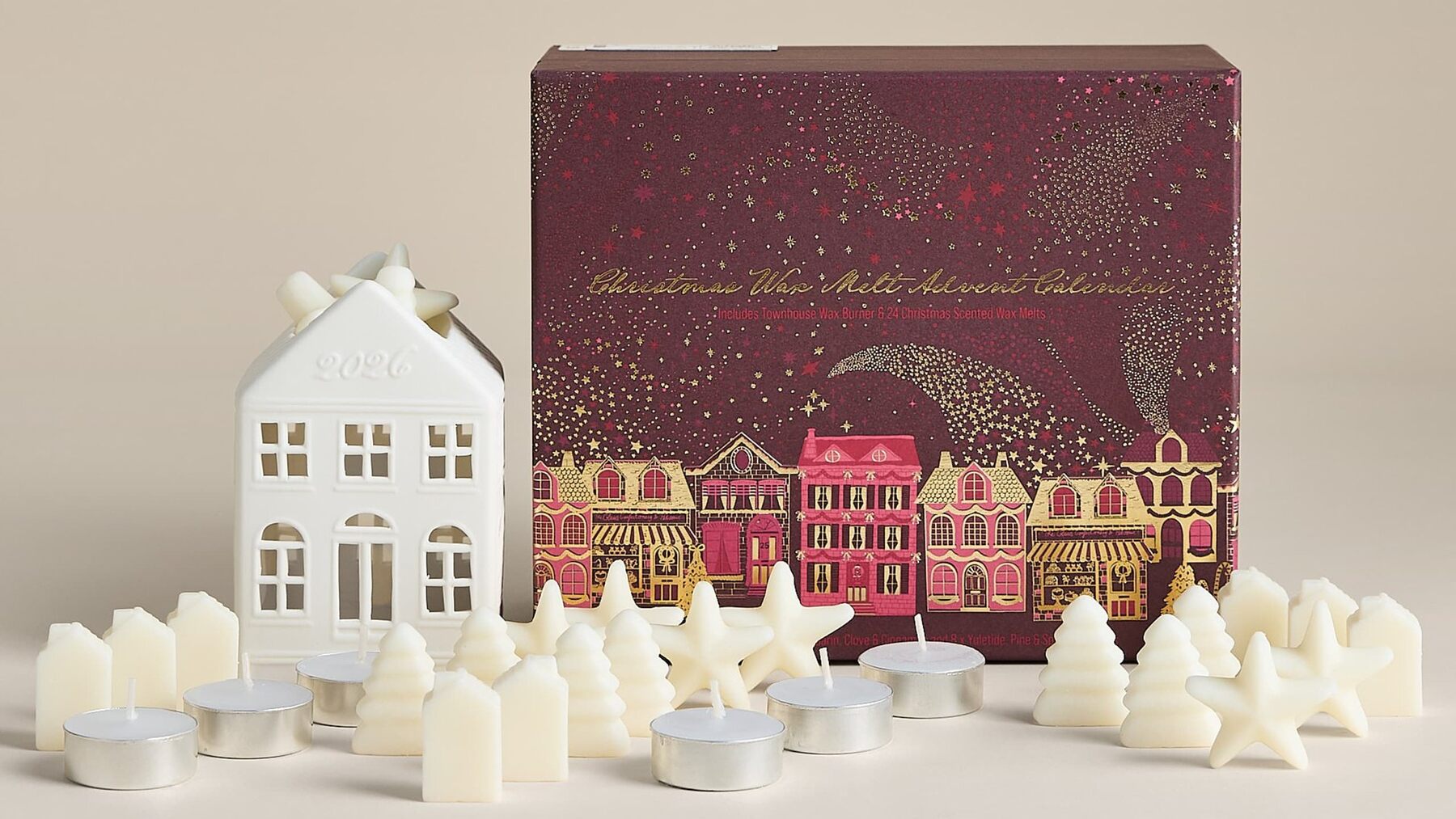 The burgundy M&S wax melt advent calendar box next to a white ceramic townhouse burner, wax melts and tealights