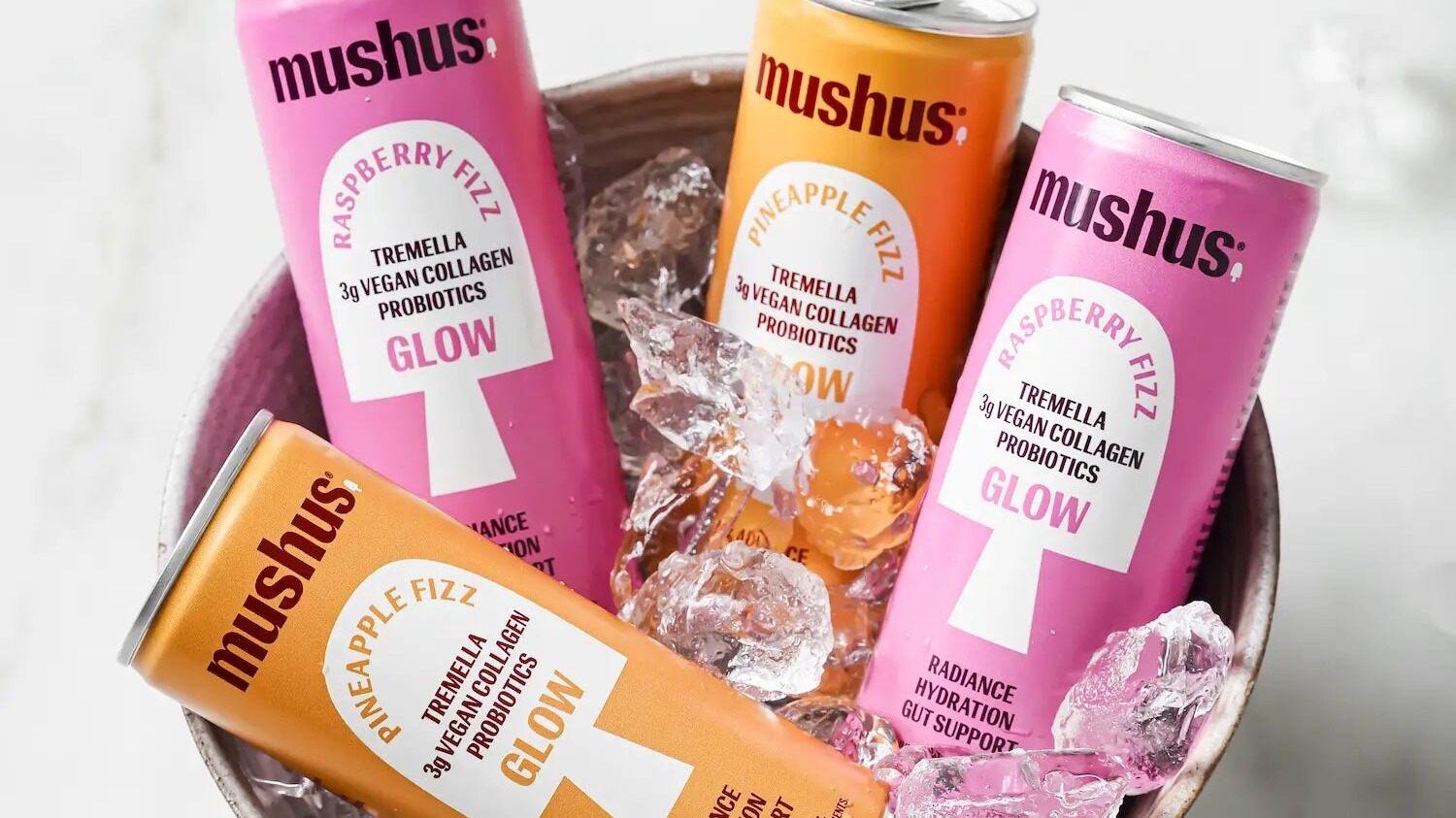 Pink Raspberry Fizz and orange Pineapple Fizz Mushus cans in a bowl of ice on a marble table