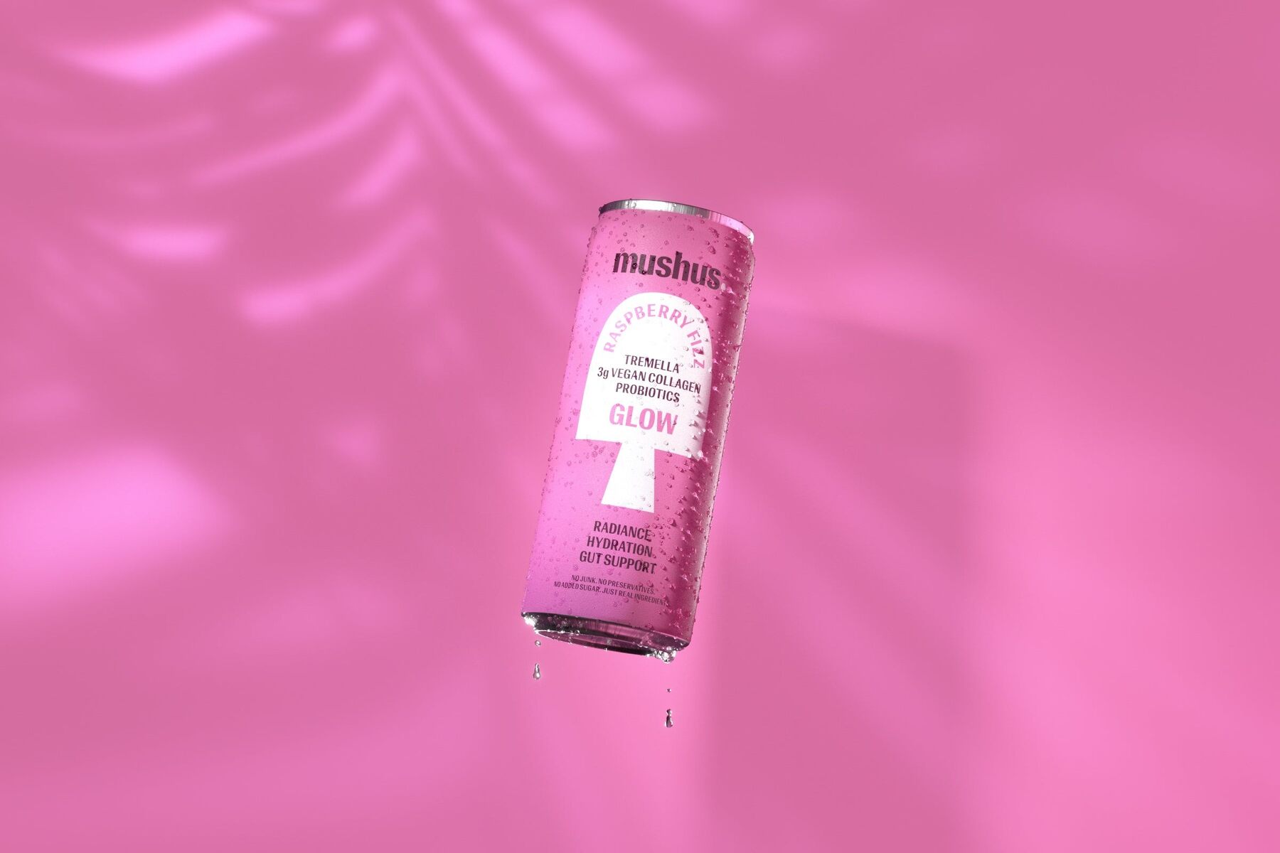 A pink can of Mushus Raspberry Fizz floating against a pink background with palm leaf shadows