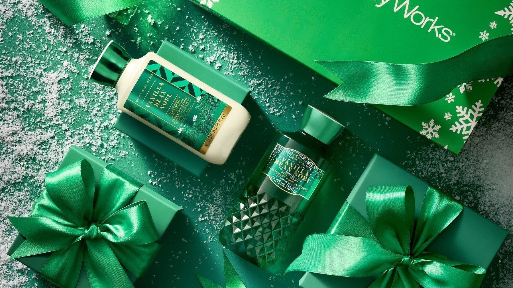 Bath & Body Works Vanilla Bean Noel body lotion and body wash among green gift boxes, ribbons and fake snow
