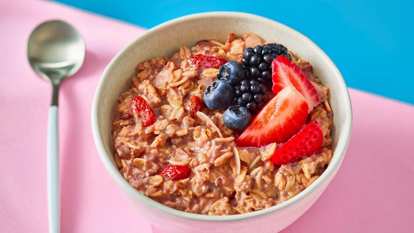 A bowl of Oat Cult overnight oats topped with strawberries, blueberries and blackberries next to a spoon