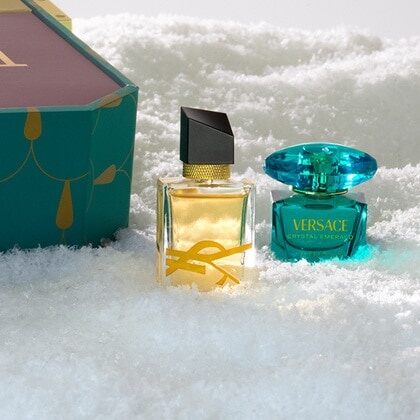 YSL Libre and a turquoise Versace perfume miniature standing in snow beside the calendar