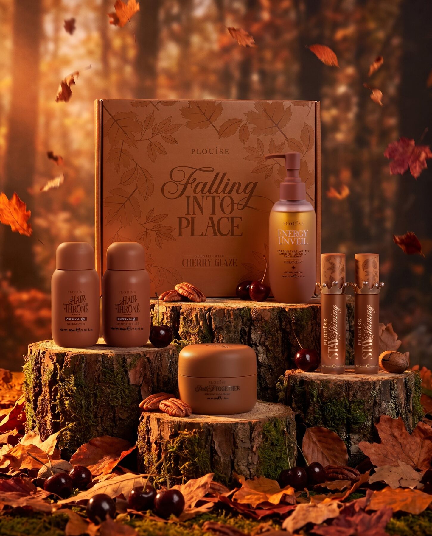 The five P.Louise October 2026 Budget Box products in Cherry Glaze, arranged on tree stumps among autumn leaves in front of the Falling Into Place box