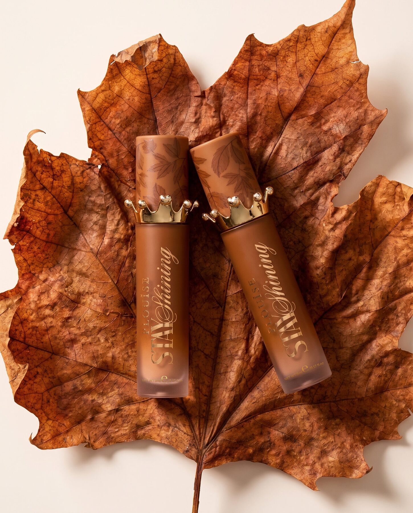 Two P.Louise Stay Shining tinted lip oils lying on a dried autumn leaf