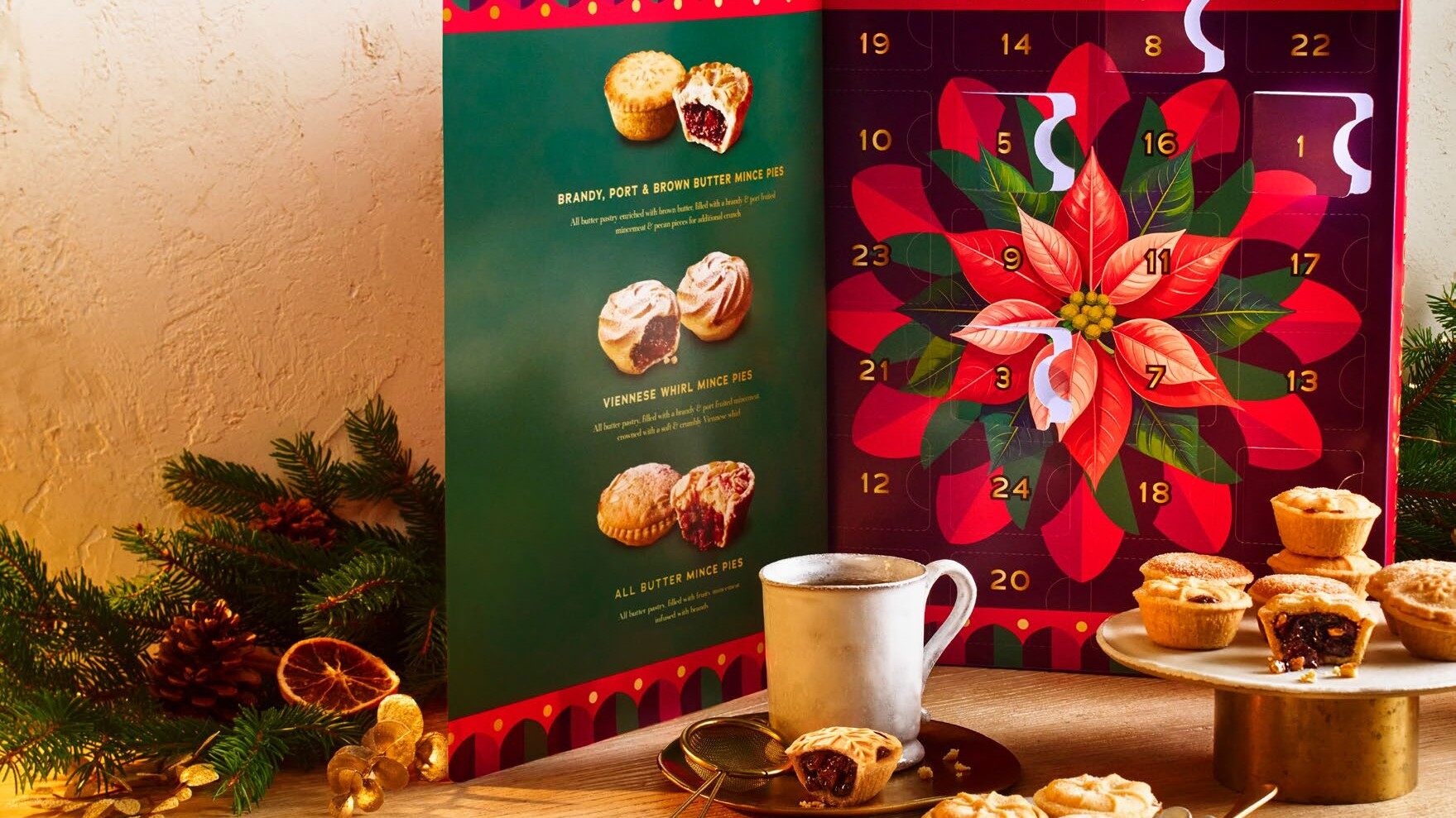 The open Sainsbury's mini mince pie advent calendar on a table with mince pies, a mug and festive greenery