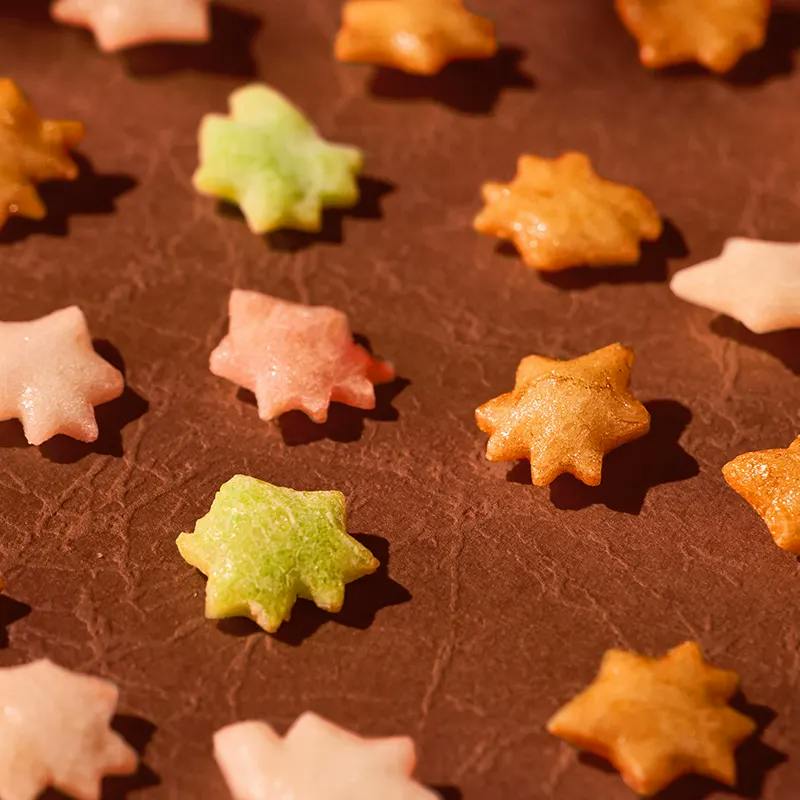 Star and maple leaf-shaped treats in pink, green and gold scattered on a brown background