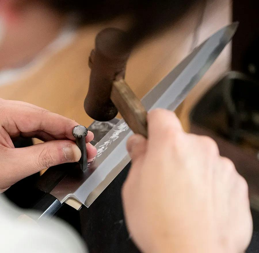 A craftsman sharpening a long kitchen knife blade by hand in a Sakai workshop