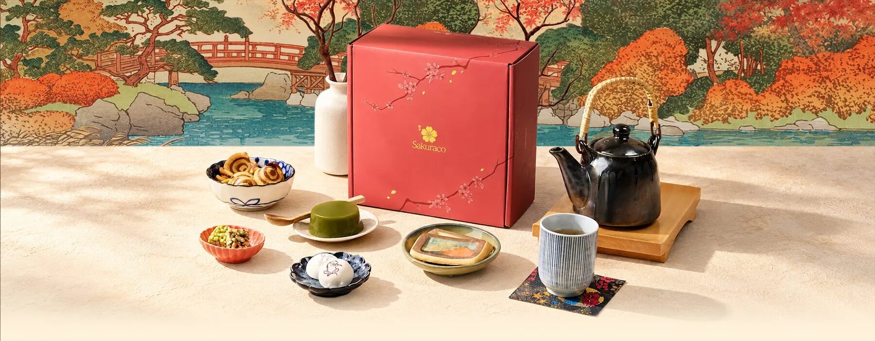 The Sakuraco Echoes of Ukiyo-e box with tea, a teapot and Japanese sweets on a table in front of an autumn ukiyo-e landscape