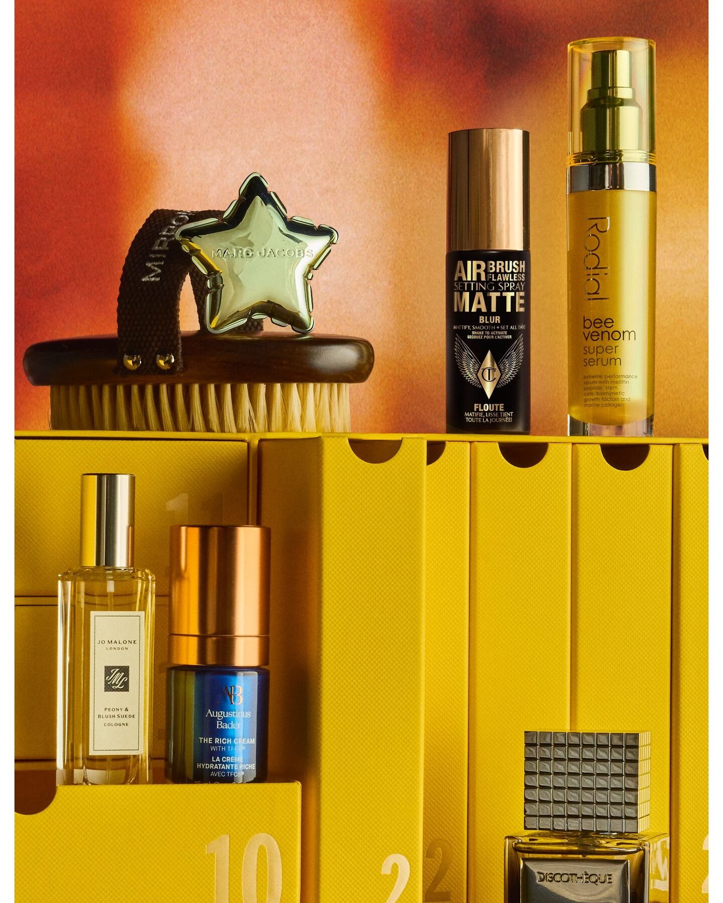 Sol de Janeiro Delicia Drench shower oil, an Isima hair mask, an Elemis cleansing balm, a Paddywax candle and other products from the Selfridges calendar on a lilac stand
