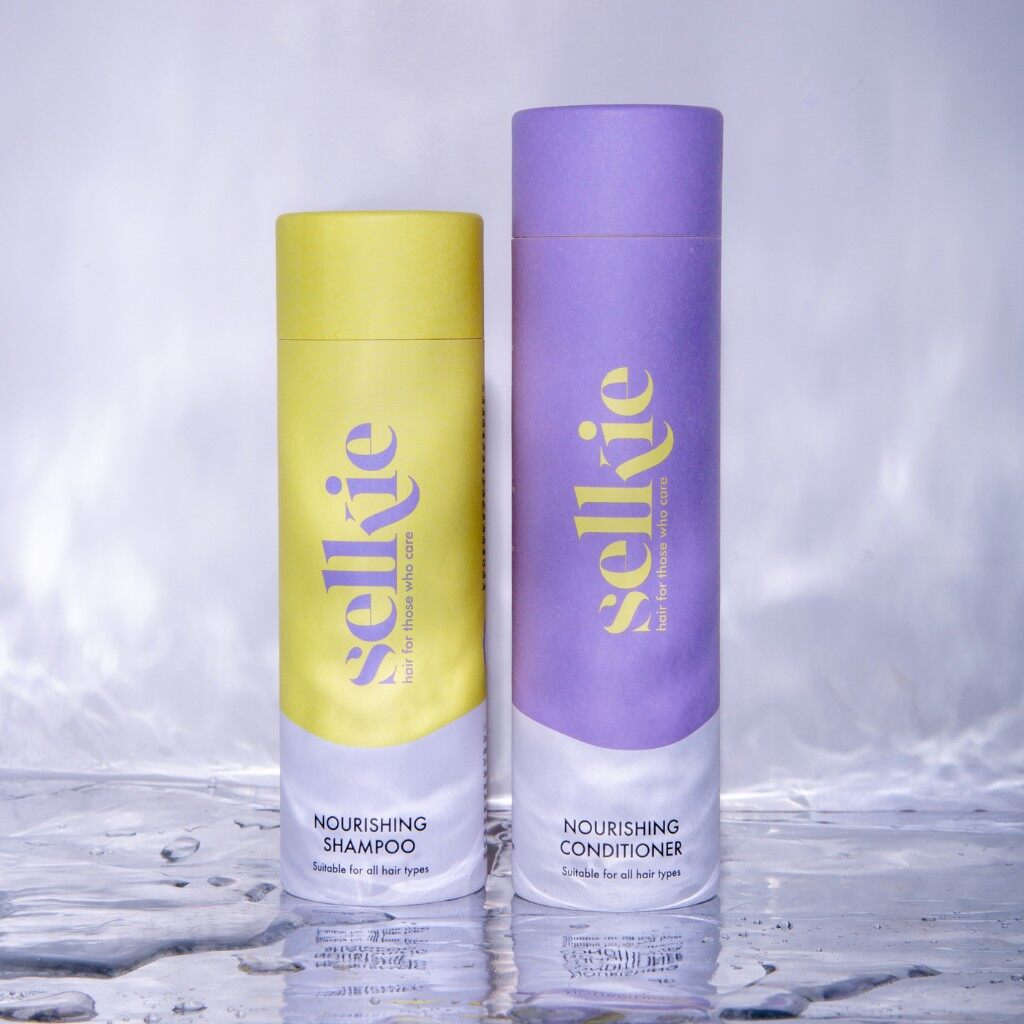 Two Selkie powder refill tubes, a yellow Nourishing Shampoo and a purple Nourishing Conditioner, standing in shallow water
