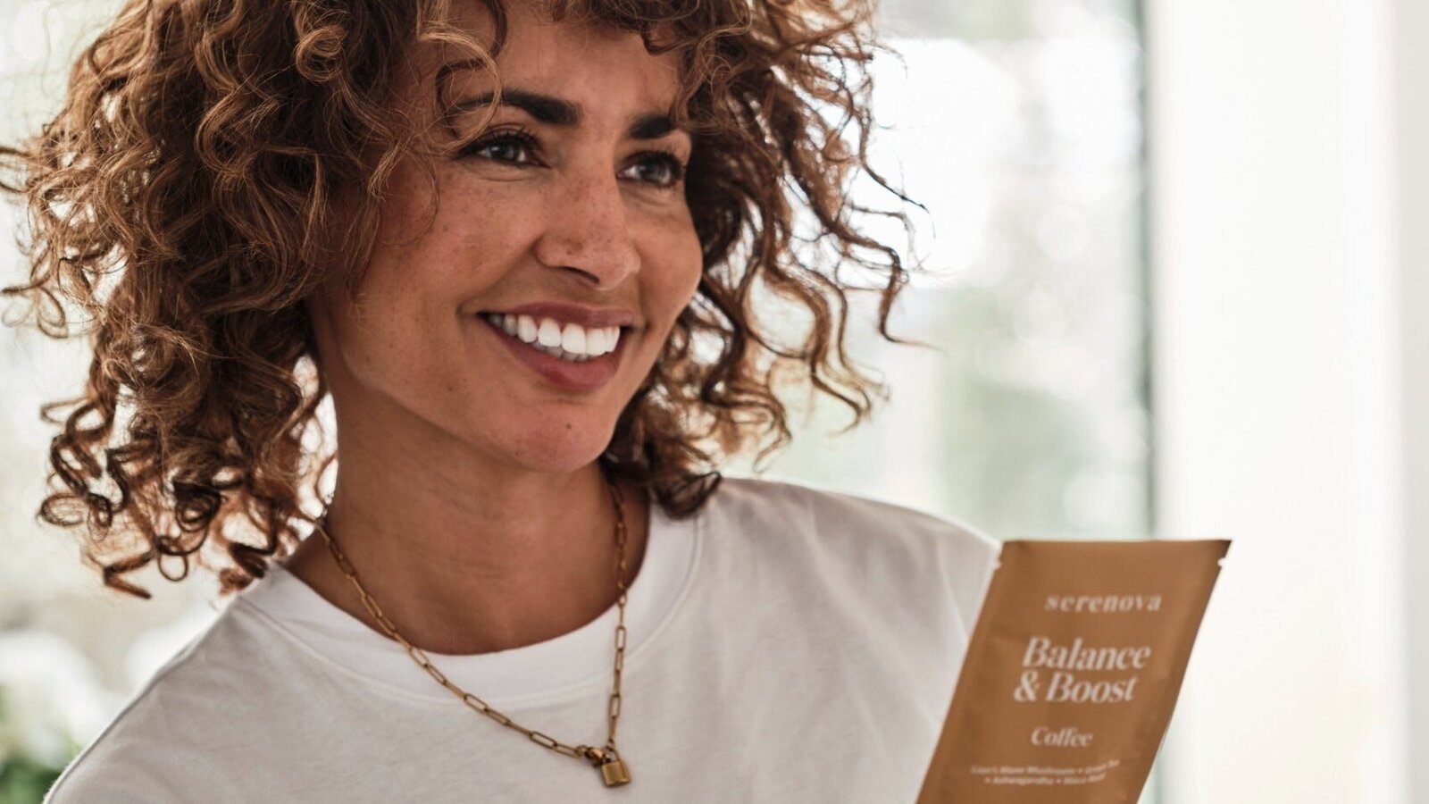 A woman smiling as she holds a Serenova Balance & Boost sachet