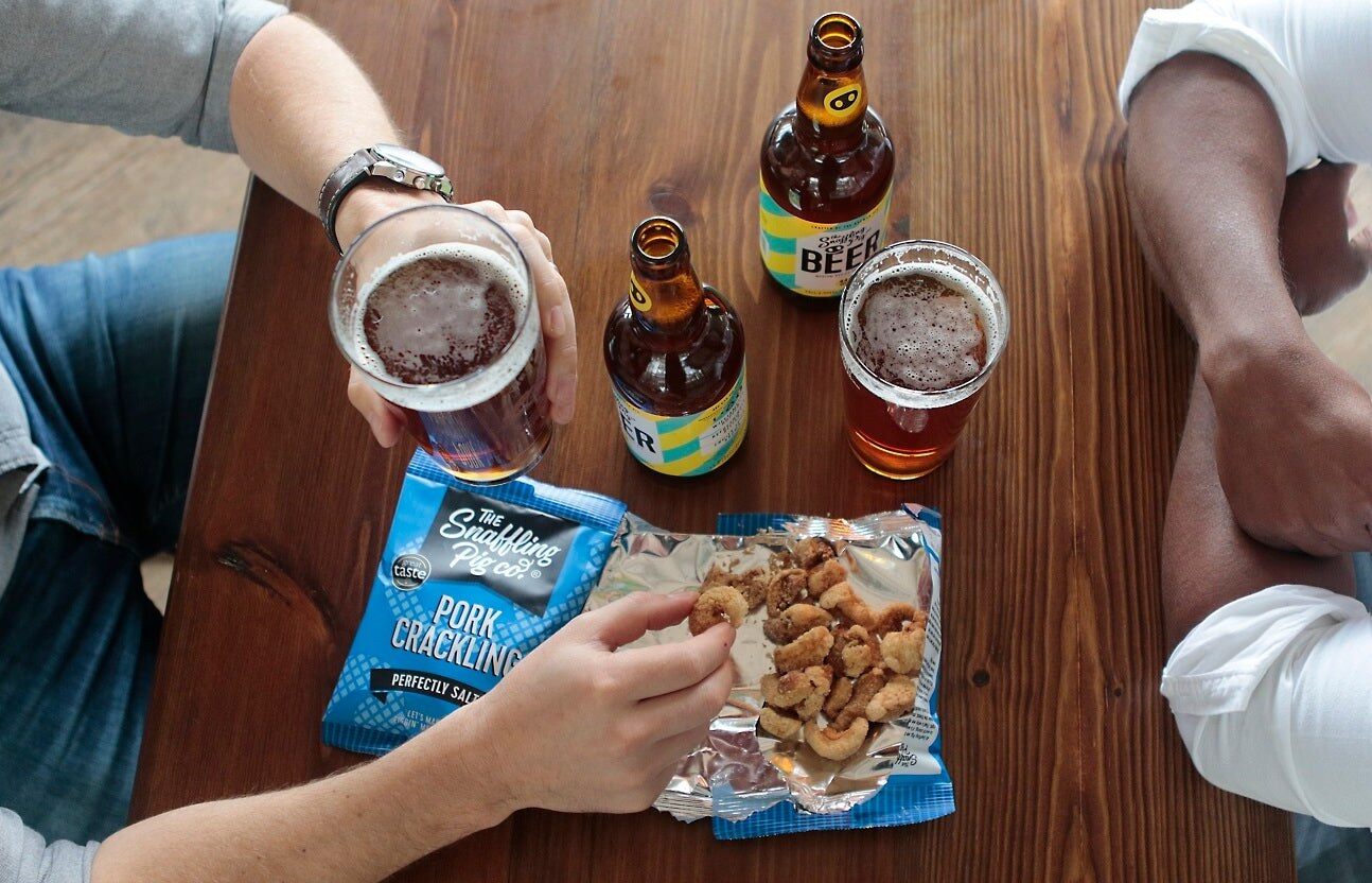 Open bag of Snaffling Pig pork crackling with bottles of beer on a pub table