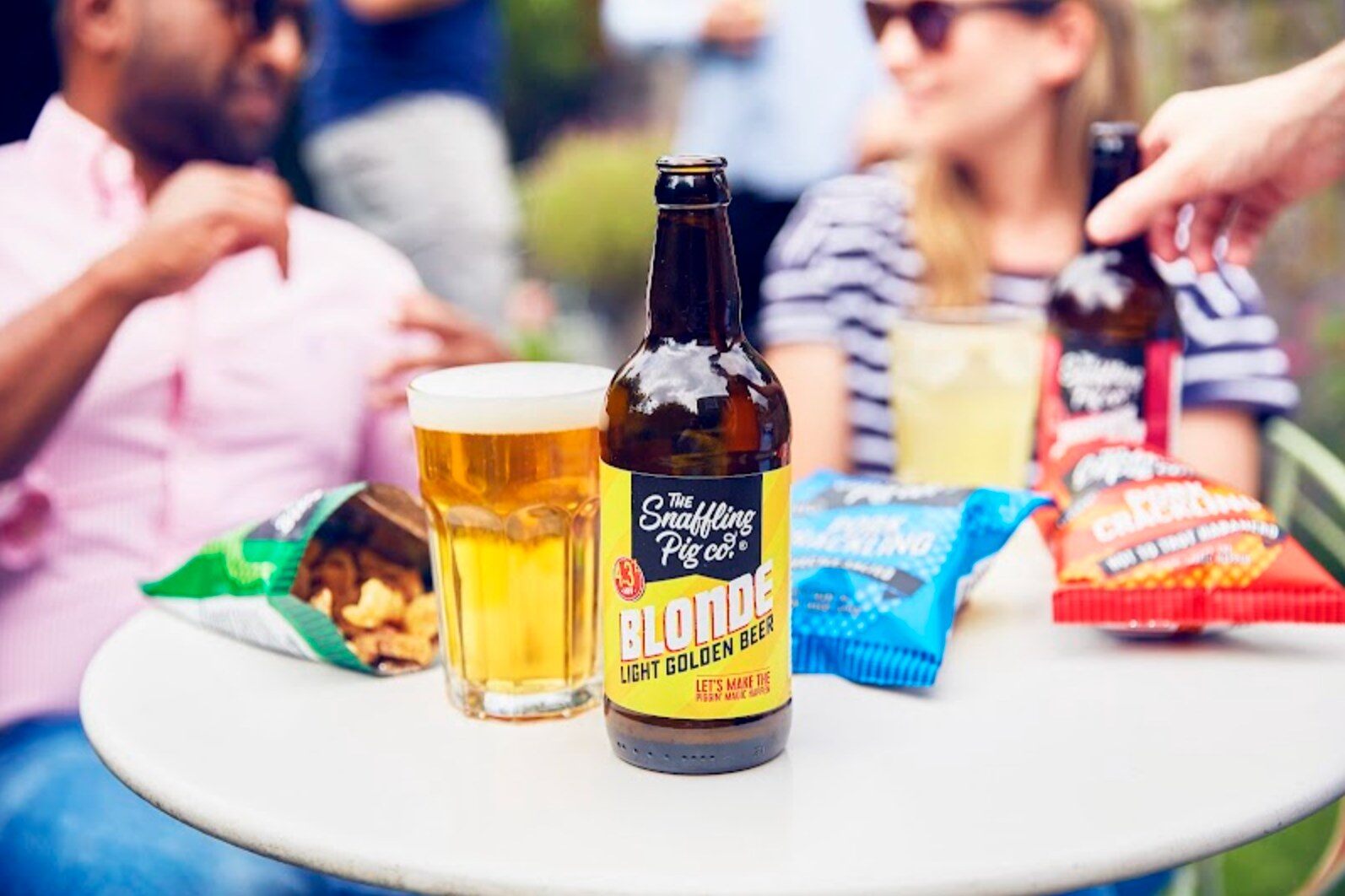 Friends sharing Snaffling Pig pork crackling and beer at an outdoor table