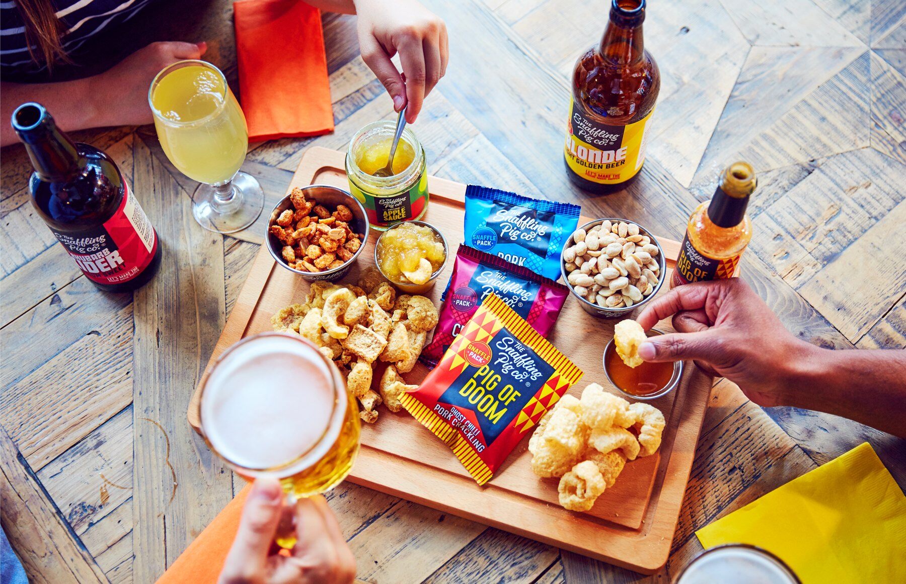 Friends sharing Snaffling Pig snacks and drinks on a wooden table