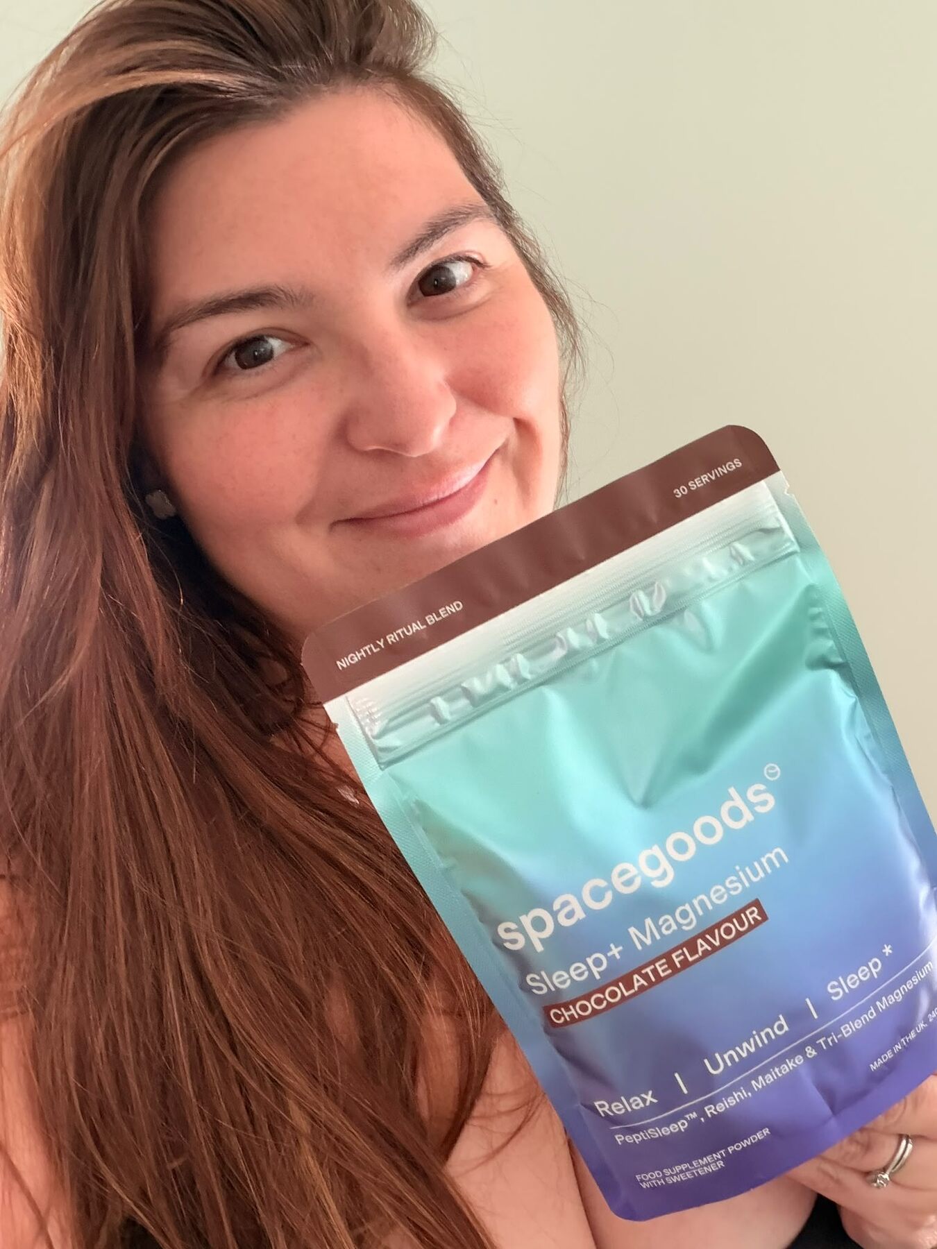 A smiling woman in pink pyjamas holding a pouch of Spacegoods Sleep+ chocolate flavour